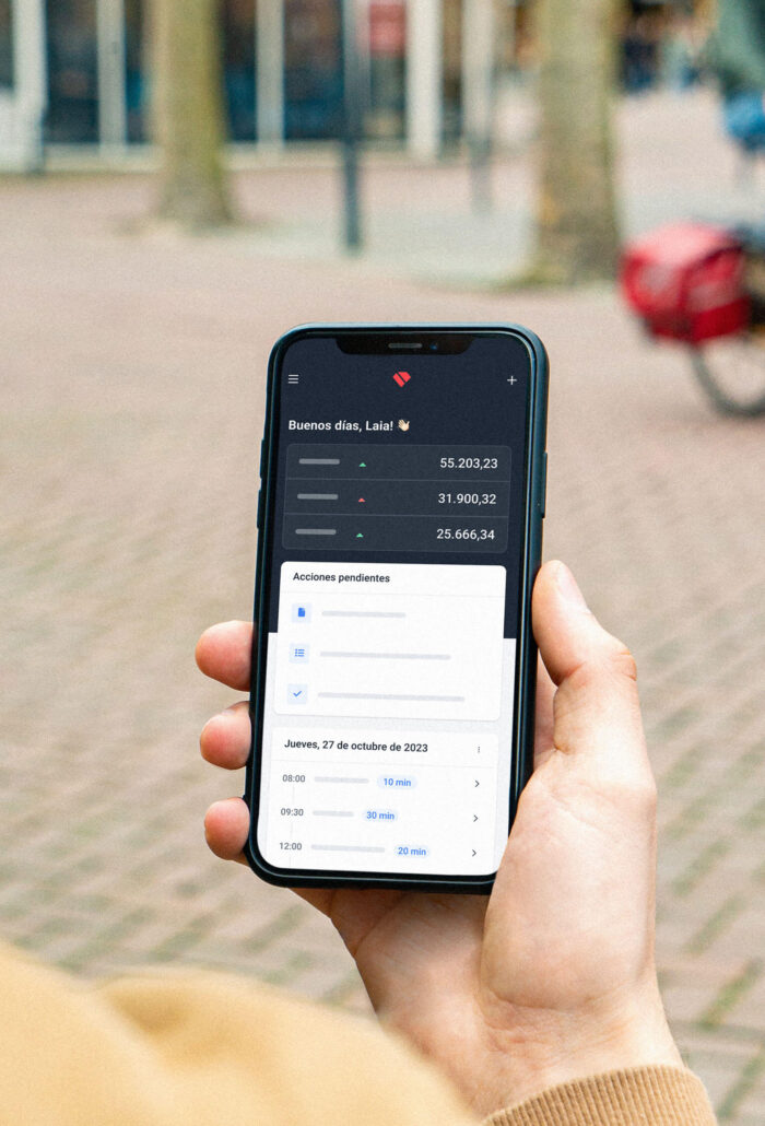 Aplicación de Holded abierta en versión mobile donde podemos ver diferentes datos proporcionados por la aplicación. El móvil esta en la mano de una persona que está en la calle